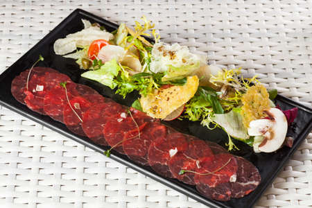 Beef carpaccio with parmesan cheese, capers and rocket salad on dark plateの写真素材