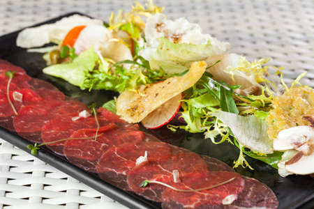 Beef carpaccio with parmesan cheese, capers and rocket salad on dark plateの写真素材
