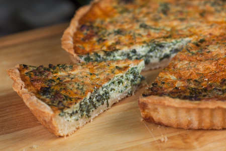 pie with cottage cheese, herbs and cheese with cut pieces on a wooden boardの写真素材