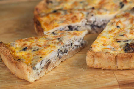 pie with chicken, mushrooms, cheese and eggs, with cut pieces on a wooden boardの写真素材