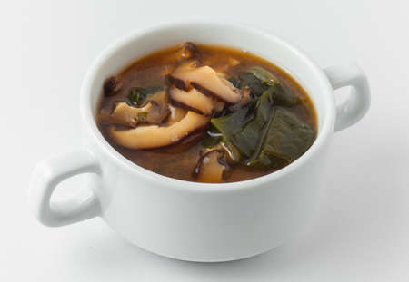 miso soup pasta dark and light, wakame seaweed, shiitake mushrooms, tofu cheese, in white tureen on white backgroundの写真素材