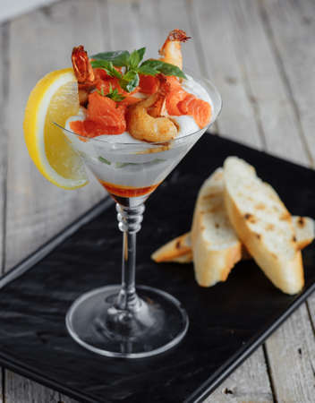 Salad shrimp cocktail sauce with salmon, lemon and basil on a wooden tableの写真素材