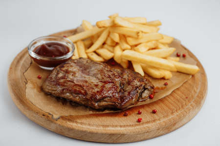 Steak with fries and sauce on a wooden tray on a white backgroundの写真素材