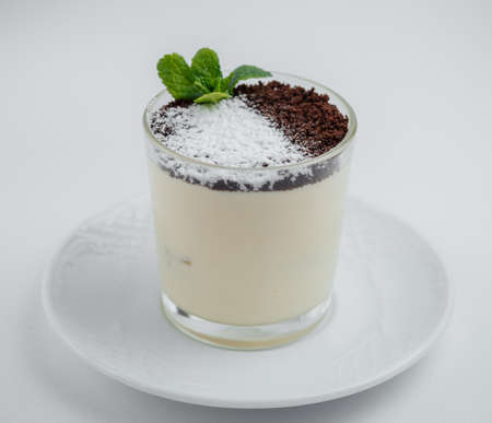 Tiramisu with chocolate chips in a glass on a white saucer on a white backgroundの写真素材