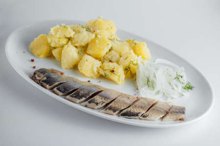 Boiled potatoes with herring, onion and dill on a white plateの写真素材