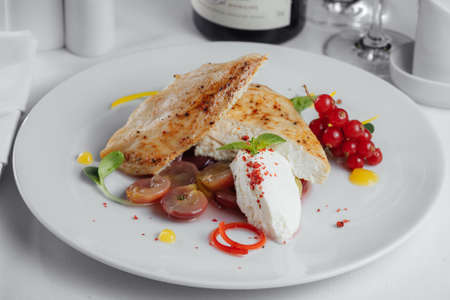 chicken with cheese, grapes, currants and pepper on a white plateの写真素材