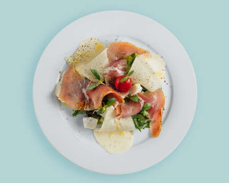 salad with prosciutto pear slices, tomatoes and herbs on a white plate, top view, topの写真素材