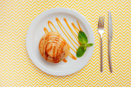 orange cinnabon in a plate with a leaf of mint in a plate top view on a yellow background. bright...