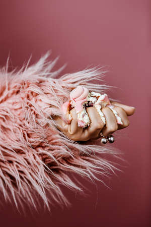 hand of a young woman crushed a pink cake with cream in a pink fur coat on a pink backgroundの写真素材