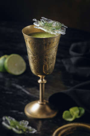 light green drink in a copper or brass metal glass, frozen parsley in ice on a dark background
