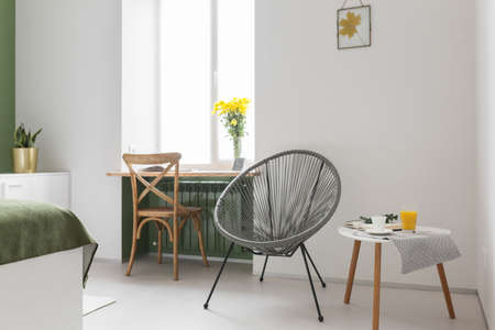 a round armchair in a bright room with white walls, a cozy space. Wooden chair and flowers on the window. Interior in a modern minimalistic style.の写真素材