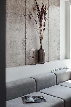 a fragment of the interior, a vertical frame with a grey sofa, a vase with dry flowers and a reed near a large panoramic window overlooking the cityの写真素材