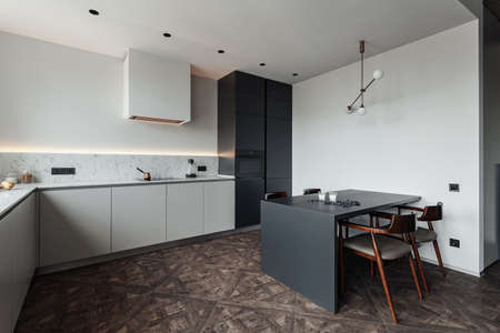 bright kitchen with dark table, convenient location of kitchen accessories and equipment, modern style, White walls, marble working surface and parquet floor. There s a glass of milk on the table and a blueberryの写真素材
