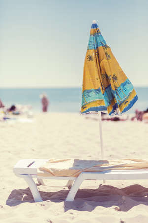 Summer vertical composition of a beach umbrella and deck chair with a carelessly thrown beach towel. Sun sand sea and beachの写真素材