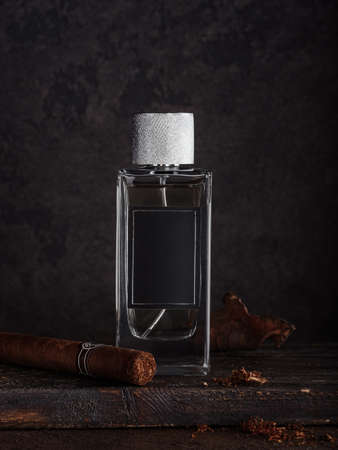 A bottle of male perfume against a dark background with a Cuban cigar and a leaf of tobacco