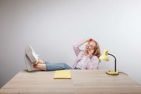 a cute girl sits with her feet on the table and talks on the phone
