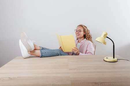 A beautiful girl sits her feet upstairs at the table and reads notesの写真素材
