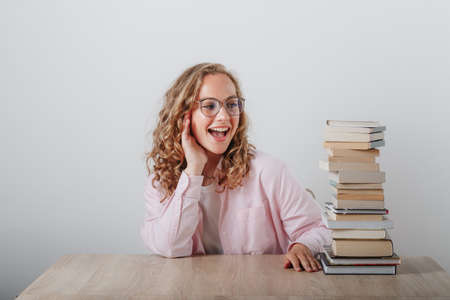 A young girl looks at a stack of books, sits at the table.の写真素材