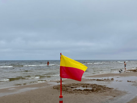 A Yellow and red beach flag, warning flag, lifesaving surf flag, rainy day in the beach, beach storm attentionの写真素材