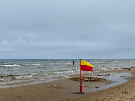 A Yellow and red beach flag, warning flag, lifesaving surf flag, rainy day in the beach, beach storm attentionの写真素材