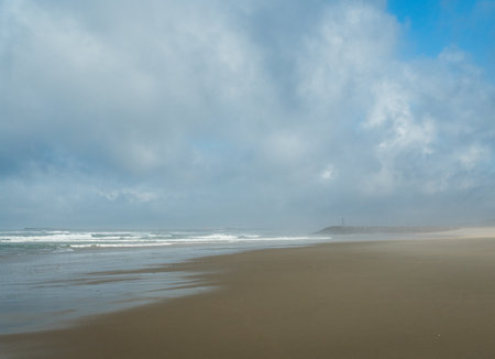 The waves of the Atlantic Ocean wash the sandy beach, the horizon is visible, the day is overcast.の写真素材