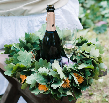 A solstice oak wreath with yellow flowers woven into it, placed on a chair and a champagne bottle with a filled glass.の写真素材