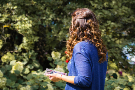 From the back, a woman with long brown curly hair, blue jacket, holding a greeting card is standing...