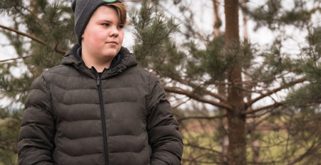 A young boy stands in the early spring countryside, dressed in a brown jacket and gray hat.の写真素材