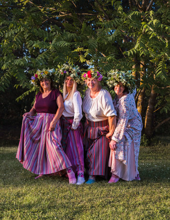 On the evening of the summer solstice, women show off their crowns on their heads and colorful, ornamented stockings on their feet. Outdoors in the park.の写真素材