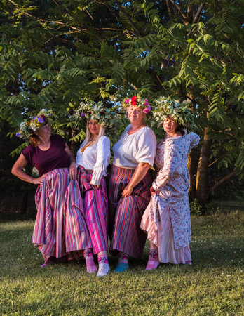 On the evening of the summer solstice, women show off their crowns on their heads and colorful, ornamented stockings on their feet. Outdoors in the park.の写真素材