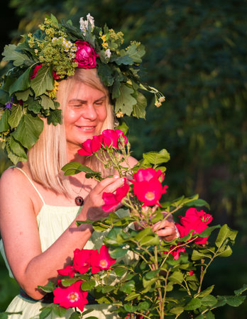 A woman in a yellow dress, with blond hair and a beautiful wreath of meadow flowers on her head, bathed in the evening sun on the evening of the summer solstice.の写真素材