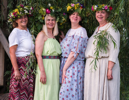 Four women, adorned with homemade wreaths, stand in the garden on a summer solstice evening.の写真素材