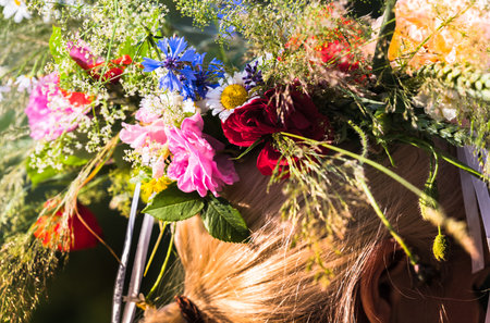 Summer solstice wreath of wild and garden flowers for a girl with blond hair and a braid on her head, handmade, individual parts in focus, summer dayの写真素材