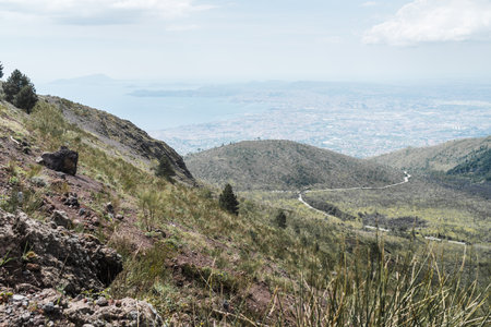 Naples, Italy - 04.28.2025: The slopes of Mount Vesuvius and the access road to a parking lot on the outskirts of Naples; in the background is the city and bay shrouded in haze.の写真素材