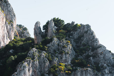 Capri, Italy - 04.29.2025: view of a white mountain range formation, with two sharp protrusions; partial vegetation of trees and shrubs.の写真素材