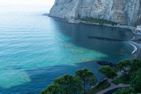 View of the bay with blue waters near the rocky coast. Small beaches and stone piers.