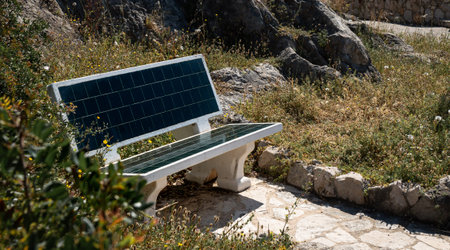 A concrete bench to sit down and relax; black tile finish for the seat and backrest; sunny day, rocky environment with grass.の写真素材