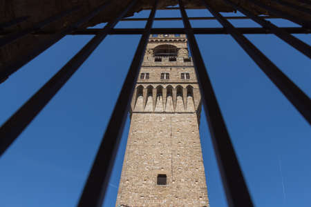 Italy, Florence - May 18 2017: the view of the Arnolfo Tower from a narrow window with iron grid of Palazzo Vecchio on May 18 2017 in Florence, Tuscany, Italy.のeditorial素材
