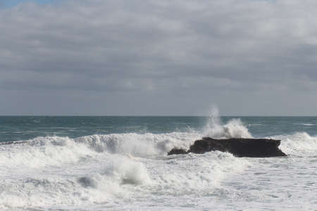 The view of the waves crashing on a group of stones.