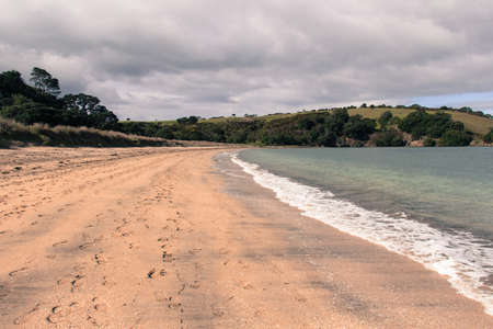 The view of coastline with sand beach, blue sea and green hill on background, Te Haruhi Bay, New Zealand.の写真素材