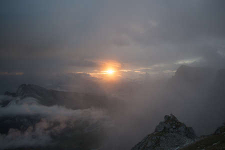 The view of sunset light through dense fog in mountains, Dolomites, Italy.