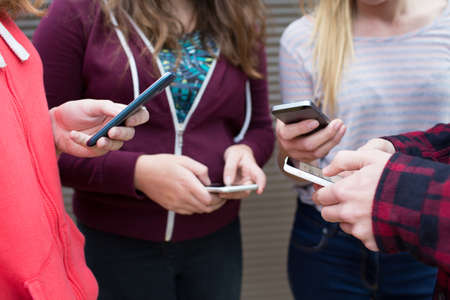 Group Of Teenagers Sharing Text Message On Mobile Phonesの写真素材