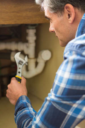 Plumber Working On Pipes Under Domestic Sink