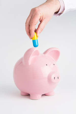 Doctor's Hand Putting Capsule Into Piggy Bankの写真素材