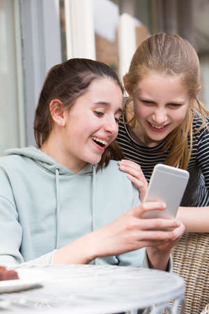 Two Young Girls At Cafe Reading Text Message On Mobile Phoneの写真素材