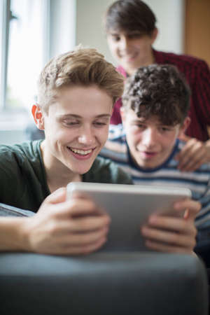 Three Teenage Boys Playing Game On Digital Tablet At Homeの写真素材