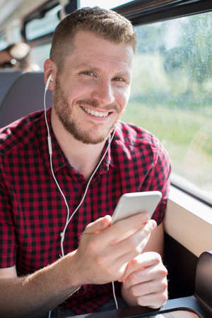 Young Man Listening To Music On Mobile Phone During Journey To Work