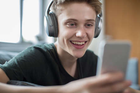 Teenage Boy Streaming Music From Mobile Phone To Wireless Headphonesの写真素材