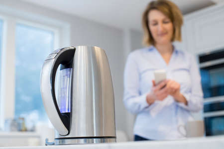Woman Controlling Smart Kettle Using App On Mobile Phoneの写真素材