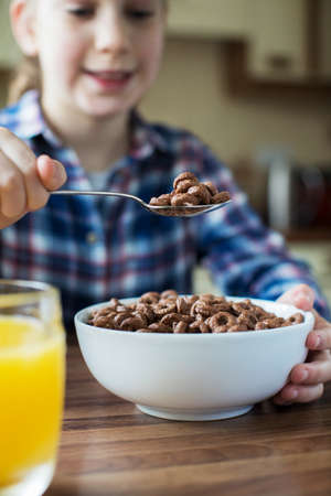Girl Eating Bowl Of Sugary Breakfast Cereal In Kitchenの写真素材
